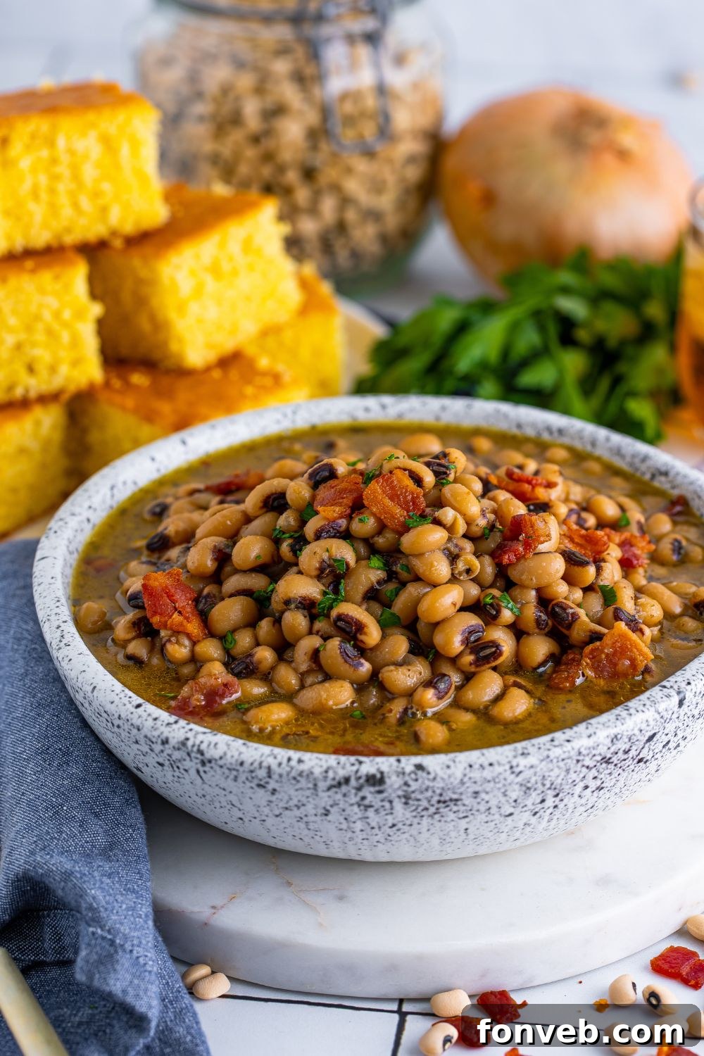Black Eyed Peas in a bowl with a side view to see peas and ingreidents in bowl. the cornbread and parsley are sitting around the bowl 