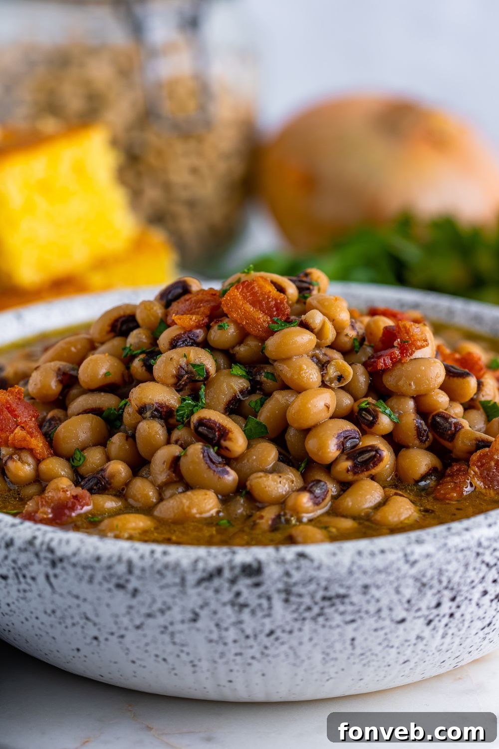 Black Eyed Peas in a bowl on the table with some ingredients and cornbread in the background 