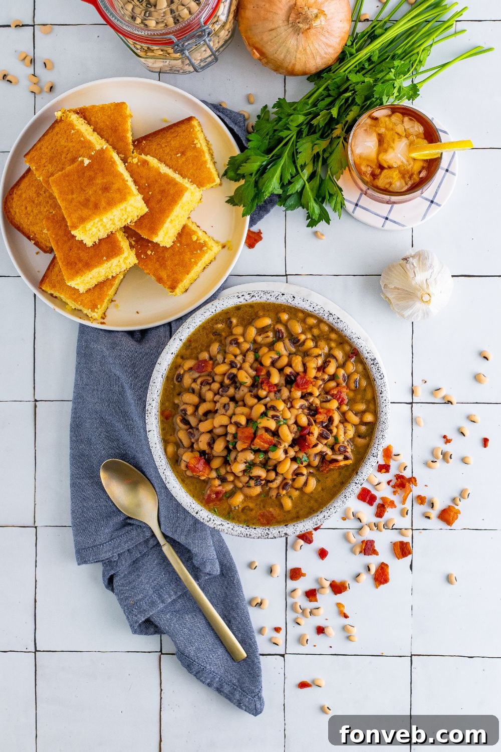 overhead look of black eyed peas in a bowl, plate of cornbread, and garnishes around plates