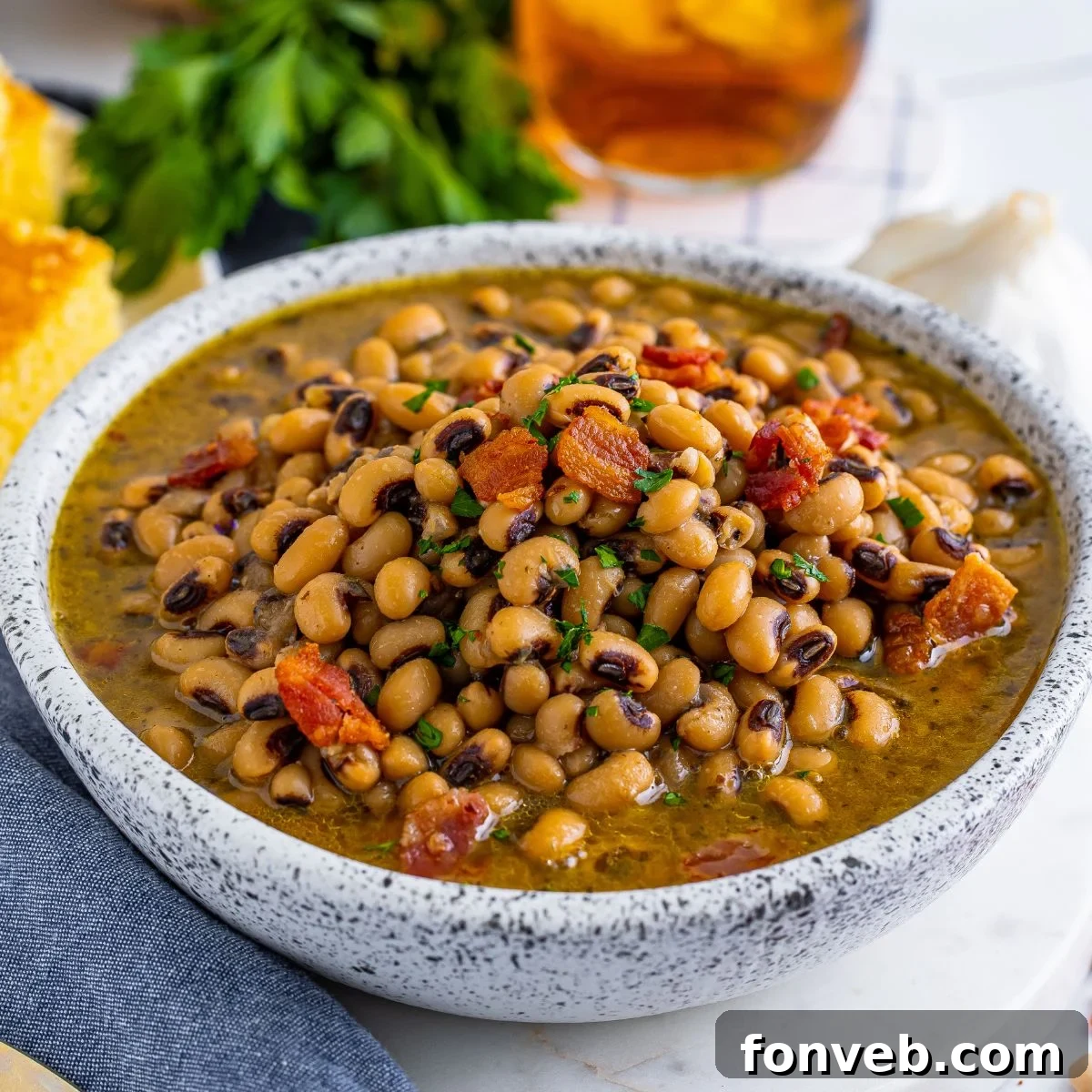Black Eyed Peas in a bowl with fresh herbs and a drink sitting behind the bowl on the table 