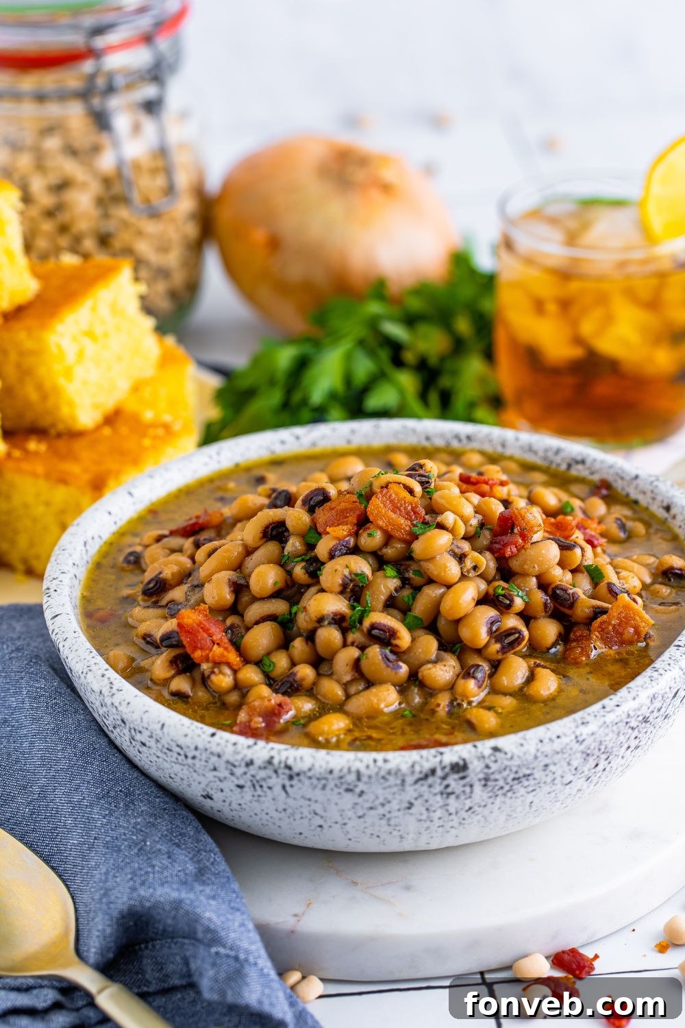 Black Eyed Peas in a bowl with cornbread, onion, parsley and a glass of tea sitting behind the bowl 