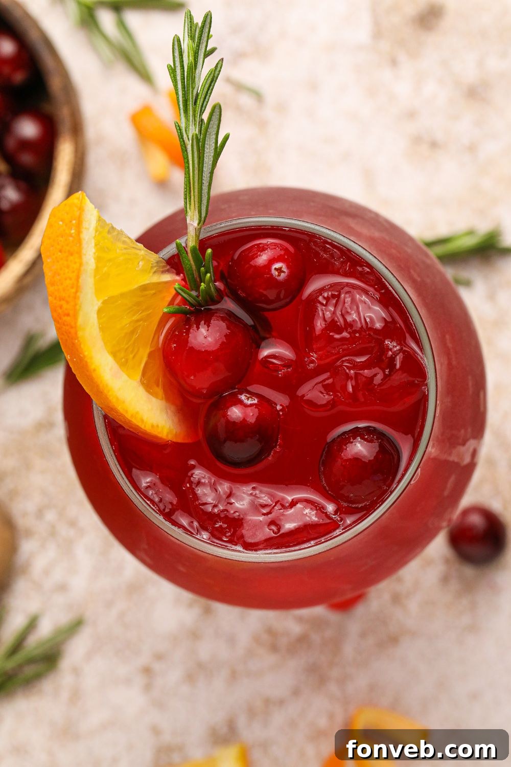 Crimson Whiskey Zing 11 Cranberry Whiskey Sour on table with an overhead look into the glass with an orange slice and cranberries in the glass with ice