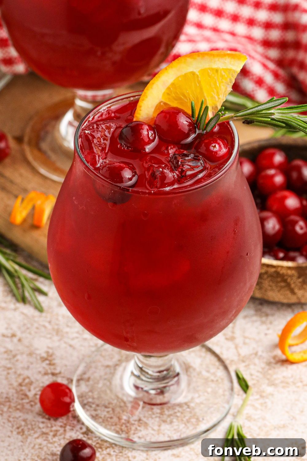 Crimson Whiskey Zing 4 Cranberry Whiskey Sour in a cocktail glass garnished with cranberries, and an orange wedge on the glass