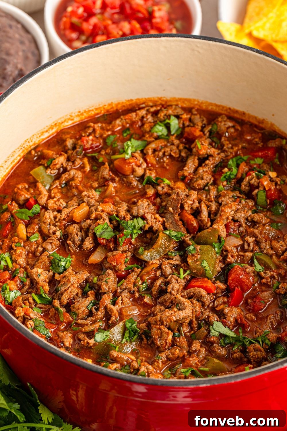 Zesty Ground Beef Medley 13 Cooked Carne Picada in a Dutch oven, surrounded by small bowls of fresh ingredients on a wooden table, suggesting a ready meal
