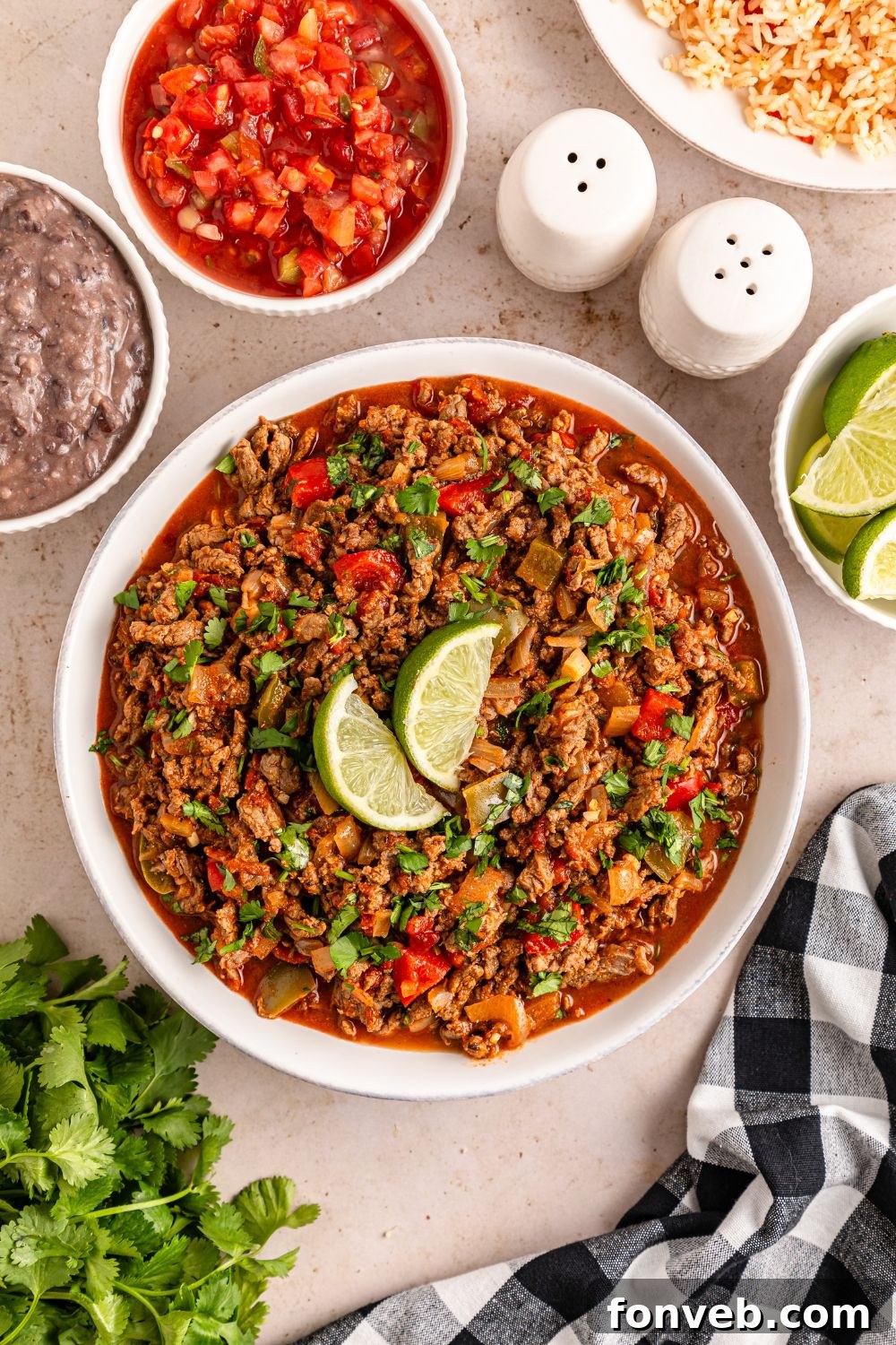 Zesty Ground Beef Medley 15 An overhead view of a bowl of Carne Picada, garnished with lime wedges and cilantro, with fresh ingredients artfully arranged around it