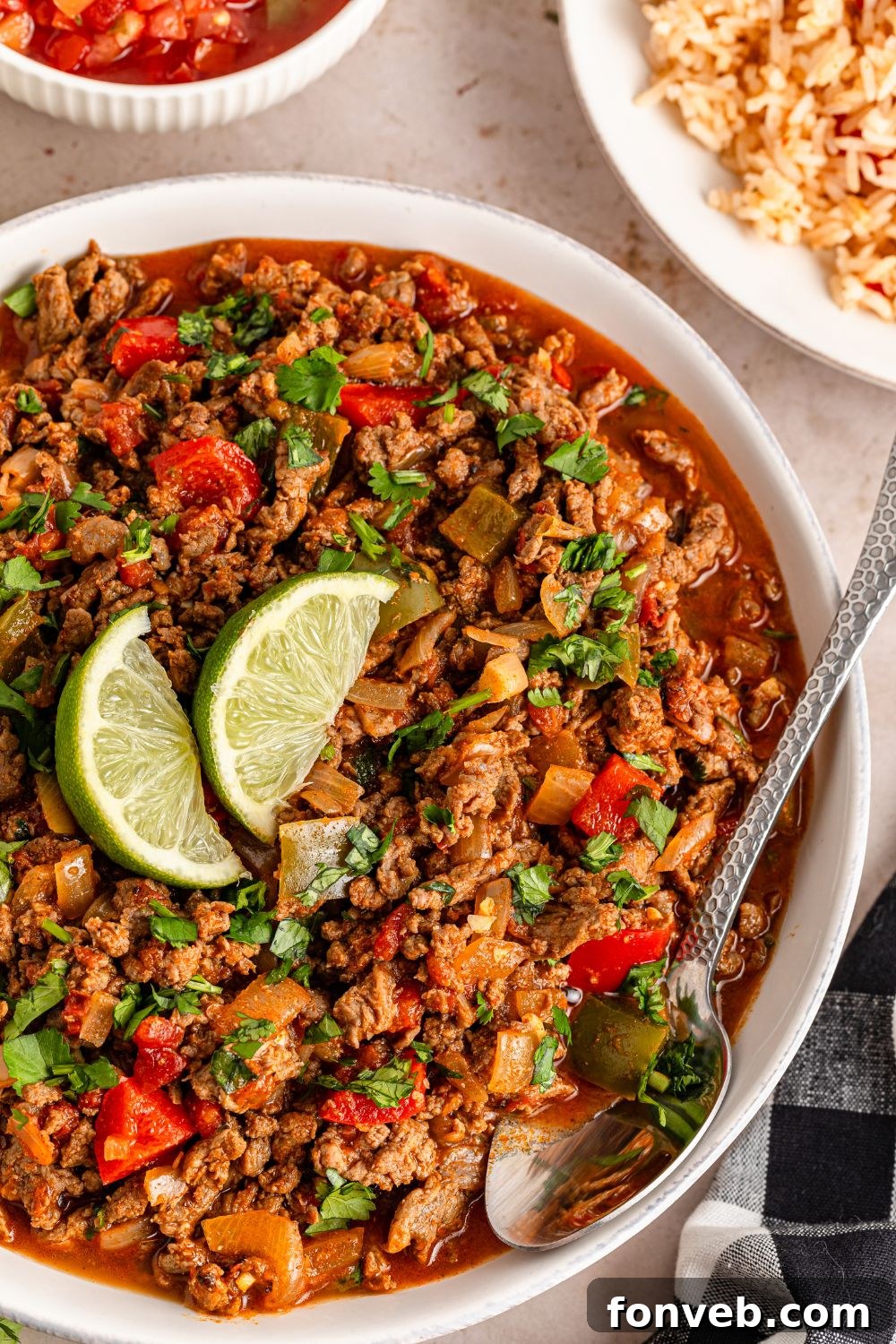 Zesty Ground Beef Medley 16 Carne Picada in a bowl, featuring a central arrangement of lime wedges and a spoon resting within the dish, ready to serve