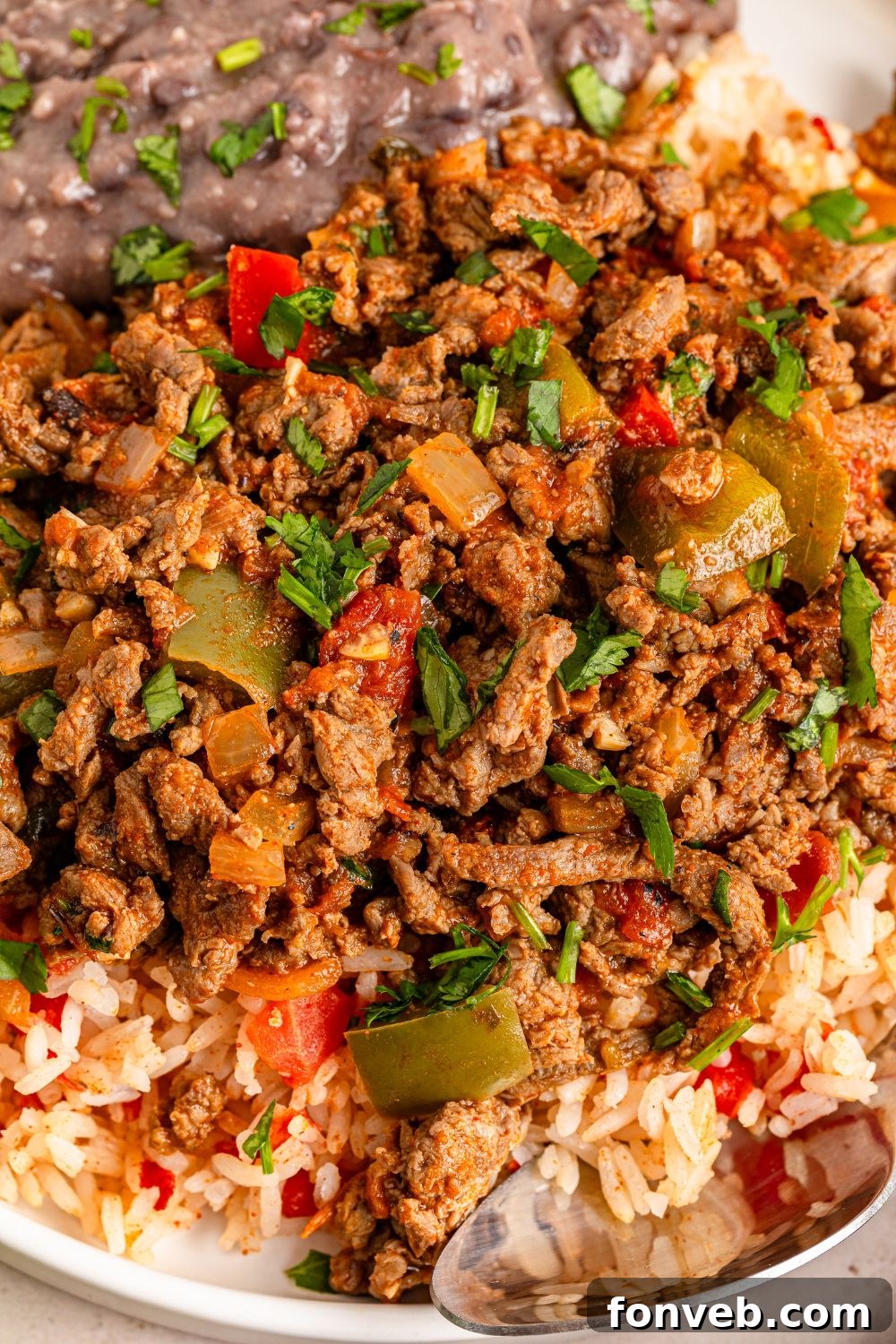 Zesty Ground Beef Medley 17 A serving of Carne Picada in a bowl, accompanied by rice and refried beans, with a spoon nearby, illustrating a complete meal