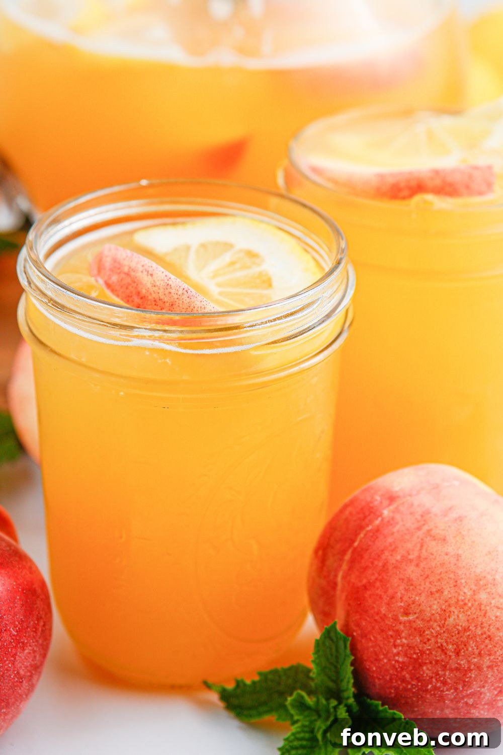 Sun-Kissed Peach Lemonade 11 Peach Lemonade in mason jars sitting on table with a whole peach sitting to the side of the glasses