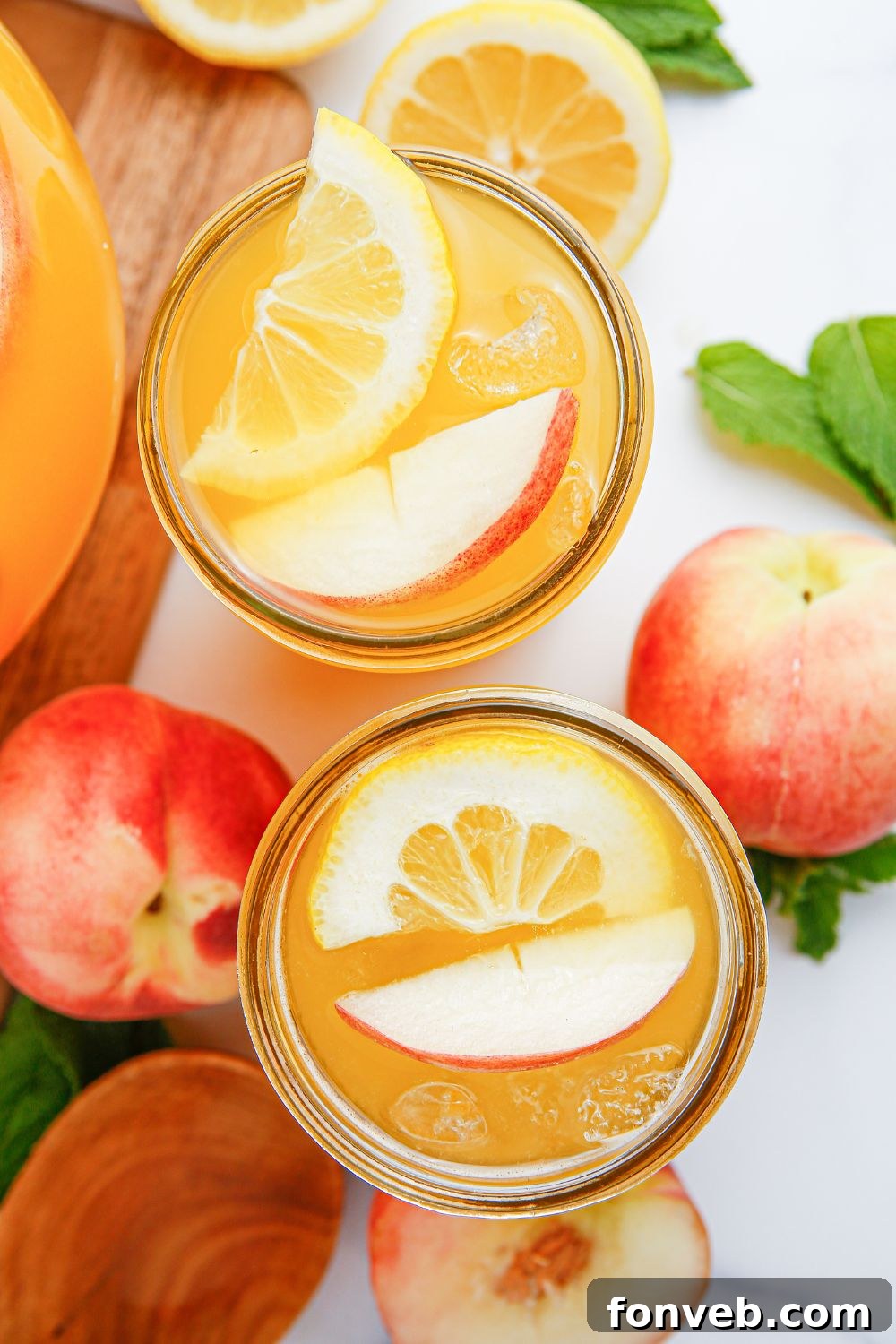Sun-Kissed Peach Lemonade 14 peach lemonade in glasses on table with fresh peaches and sliced lemons on table and mint leaves