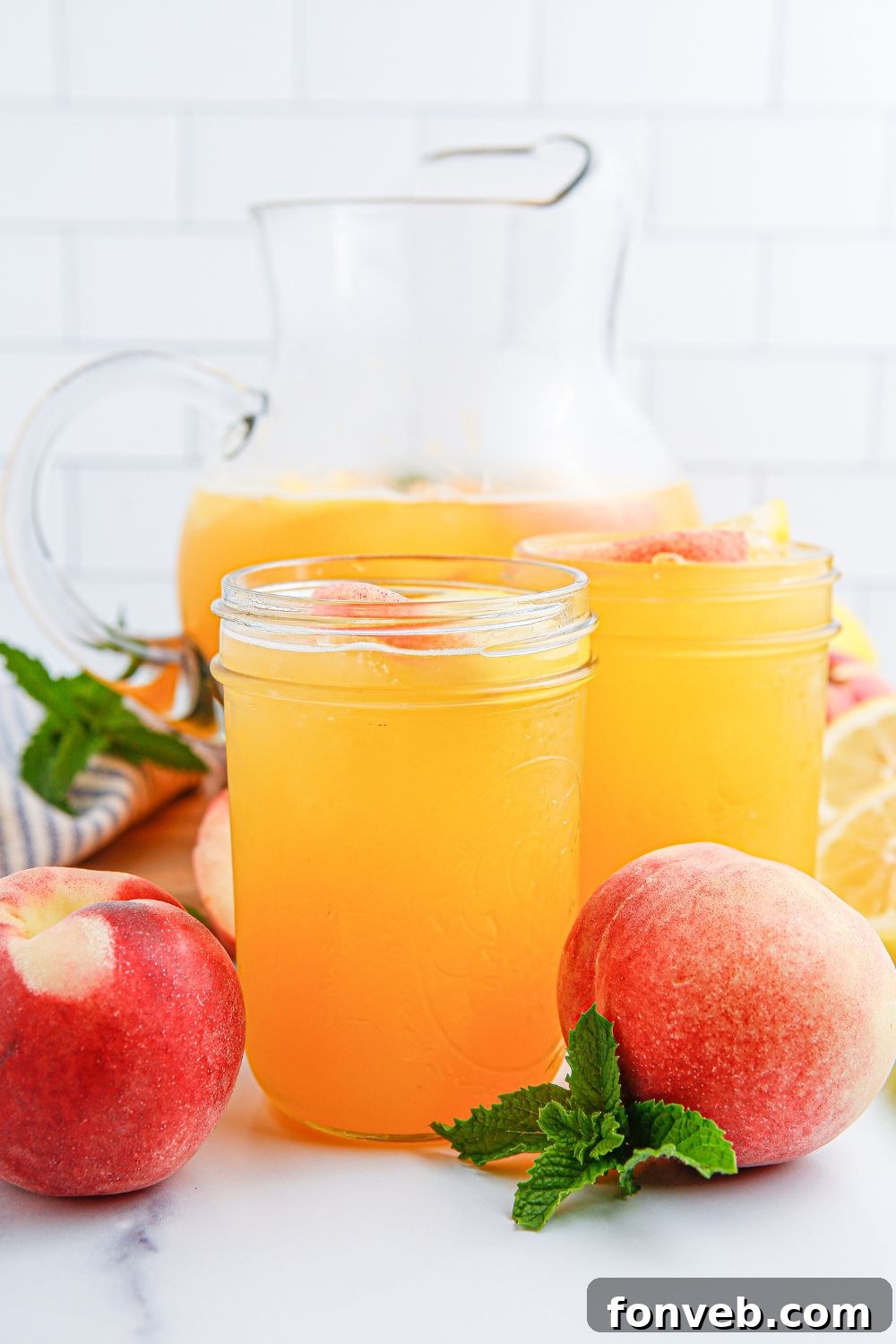 Sun-Kissed Peach Lemonade 16 fresh peach lemonade on table in glasses and a glass pitcher as well.