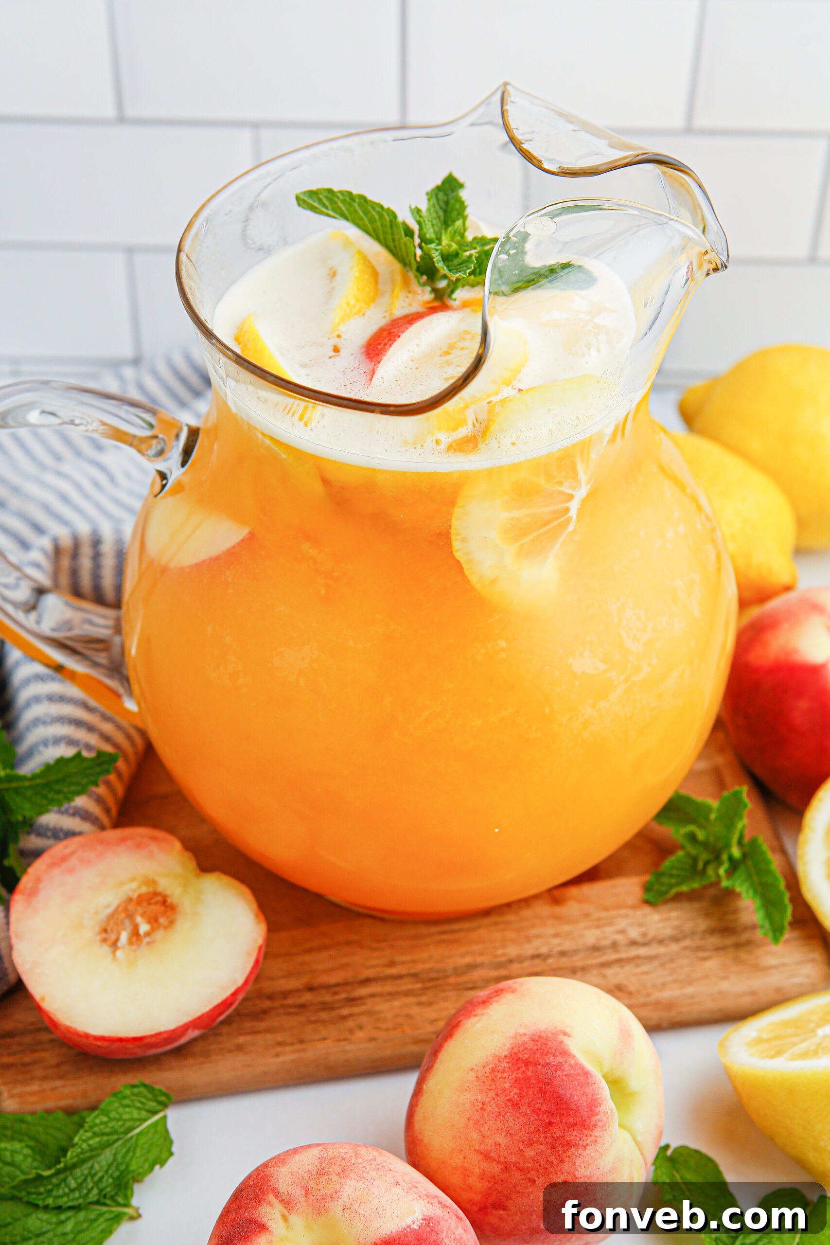 Sun-Kissed Peach Lemonade 18 Peach Lemonade in a clear pitcher garnished with peach slice and orange slices. Fresh peaches around the glass