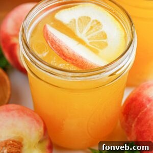 Sun-Kissed Peach Lemonade 19 Peach Lemonade in a mason jar garnished with peach slice and orange slice. Fresh peaches around the glass