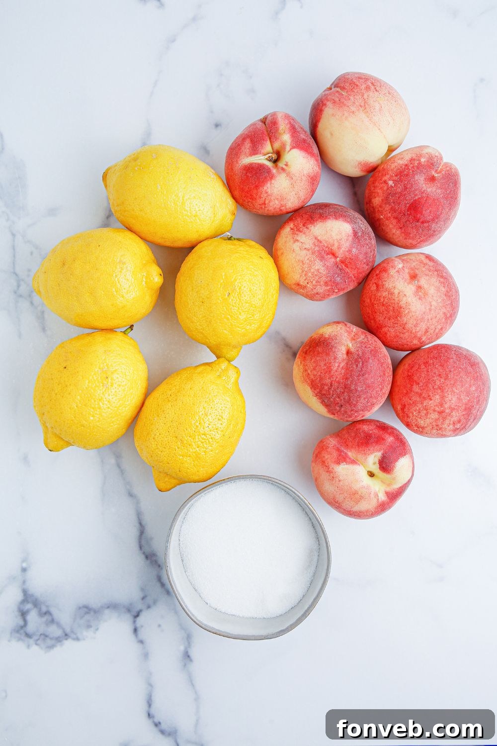 Sun-Kissed Peach Lemonade 5 lemons, peaches, and a bowl of sugar sitting on a marble countertop