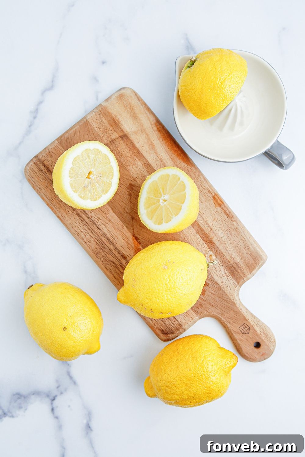 Sun-Kissed Peach Lemonade 7 fresh lemons on wooden cutting board. some are cut and a juicer is sitting next to it with half a lemon on it
