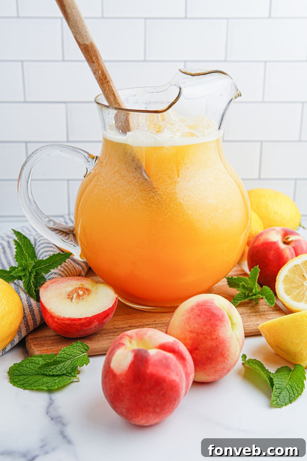 Sun-Kissed Peach Lemonade 9 wooden spoon in the pitcher of Peach Lemonade and fresh sliced peaches and lemons around the container