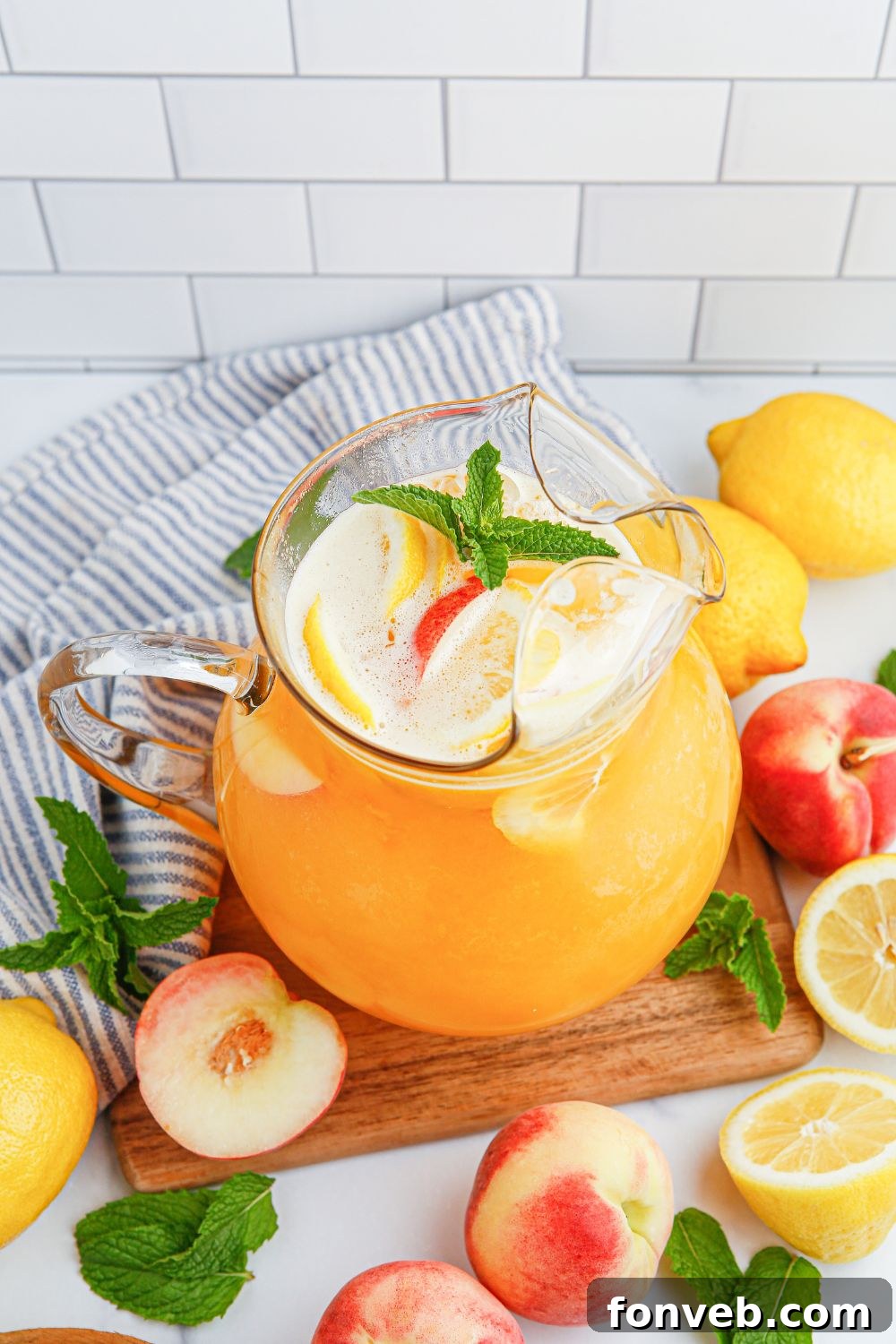 Sun-Kissed Peach Lemonade 10 Peach Lemonade in a pitcher siting on a cutting board with peaches and lemon around it on table