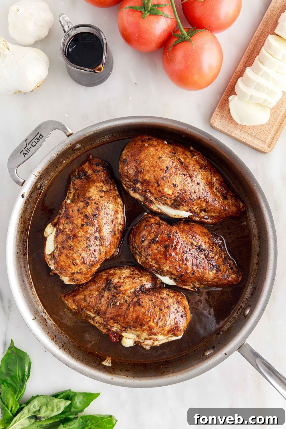 Caprese Stuffed Chicken in a skillet on a table with fresh tomatoes, mozzarella cheese, and basil leaves scattered around it