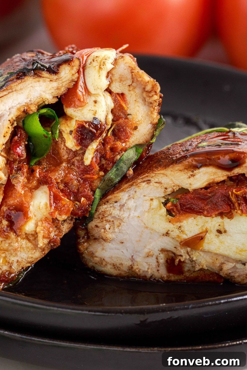 Caprese Stuffed Chicken cut in half and placed on a plate to beautifully showcase the melted cheese, tomatoes, and basil filling