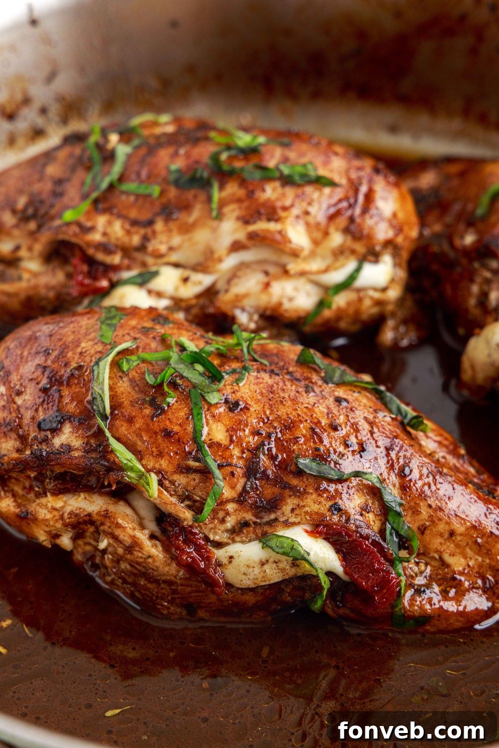 Caprese Stuffed Chicken sitting in a pan, shown from a side view, revealing its plump and golden form
