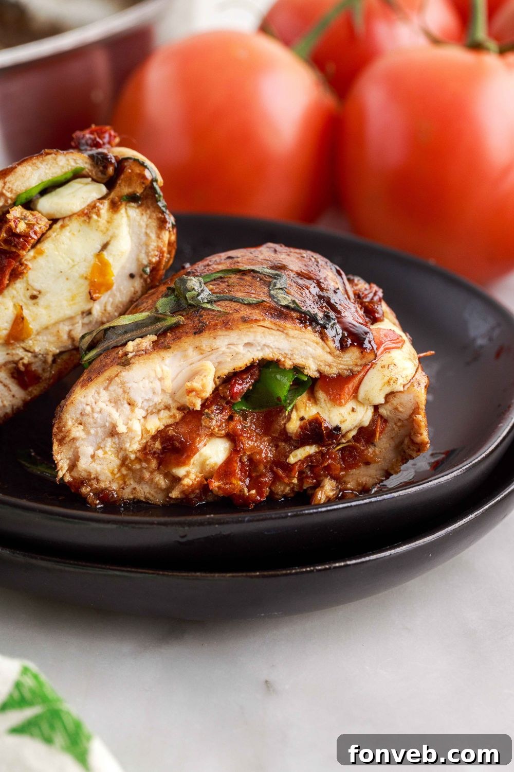 Close-up shot of a Caprese Stuffed Chicken breast on a white plate, garnished with fresh basil leaves and a balsamic drizzle