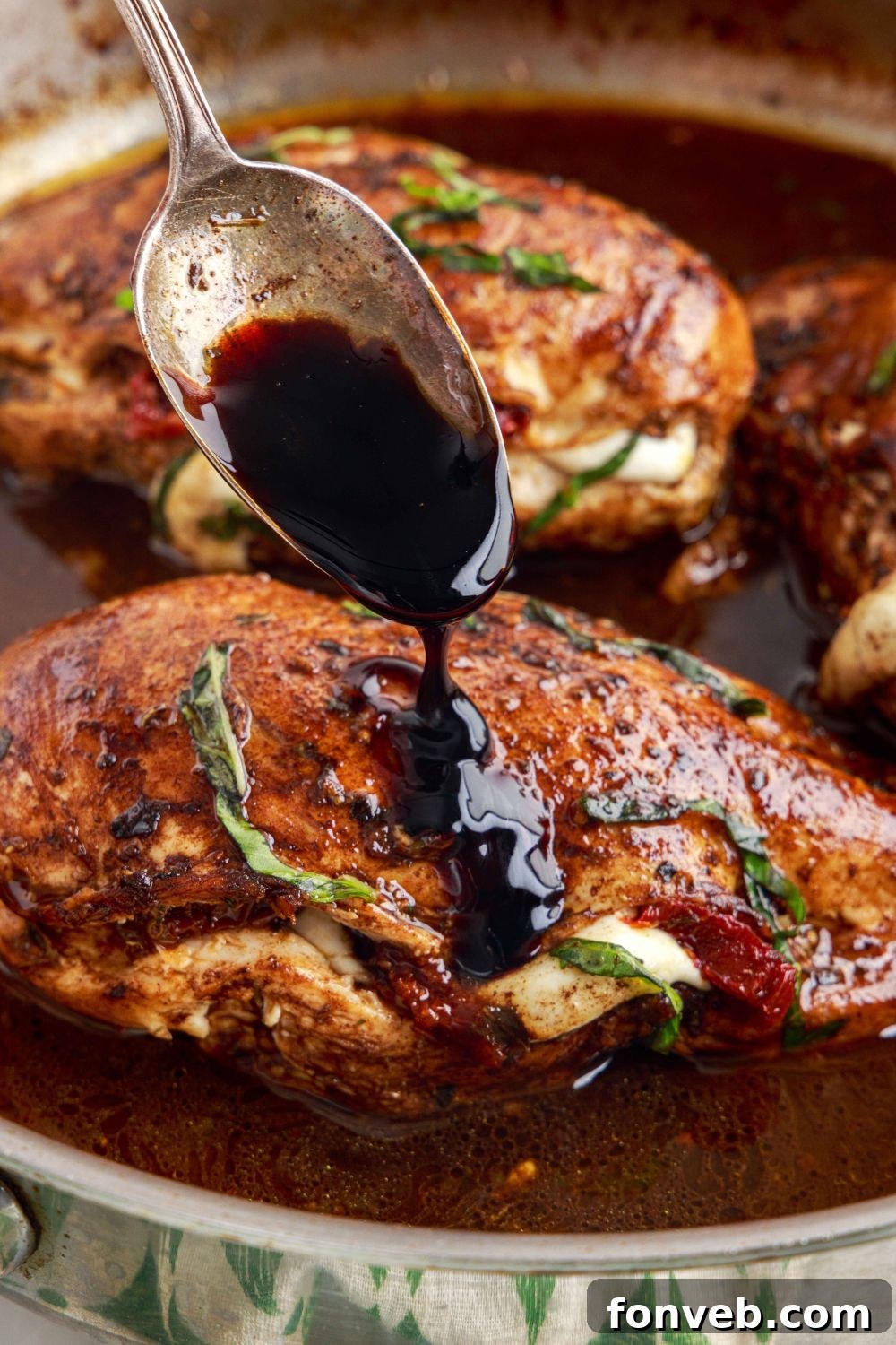 Caprese Stuffed Chicken in a pan, with a spoon drizzling balsamic glaze over the top of the chicken