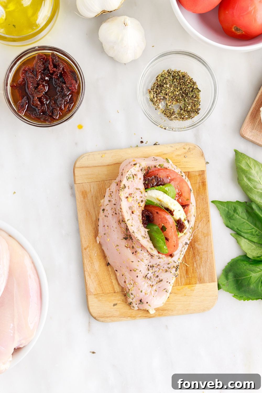Stuffed raw chicken on a cutting board, with Caprese filling visible, secured with toothpicks for cooking
