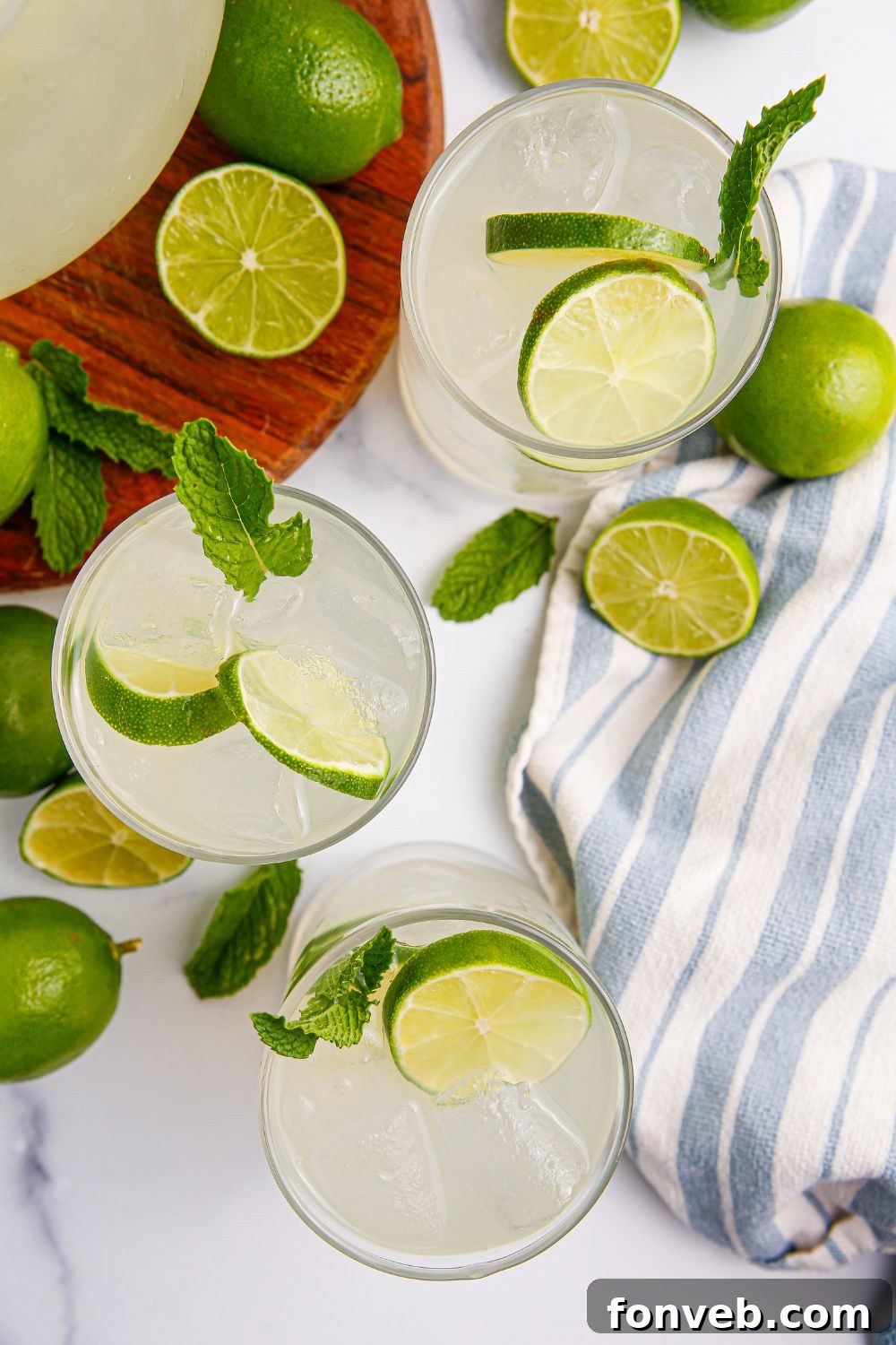 Limeade in glasses with limes scattered on table, a towel on the side