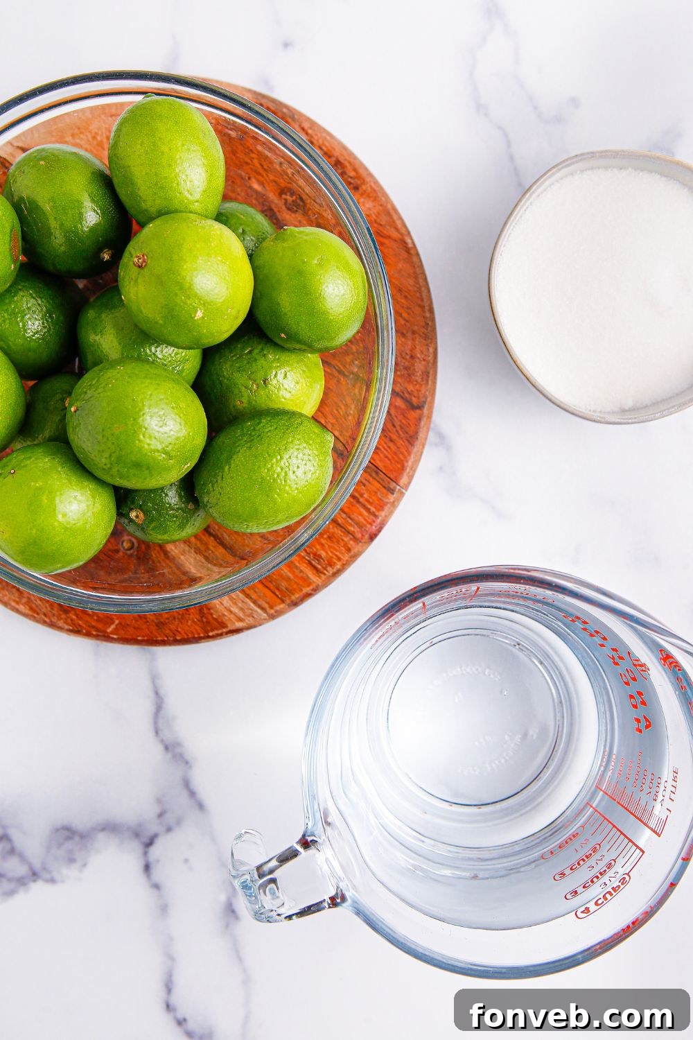 bowl of limes, water in a measuring cup, and bowl of sugar