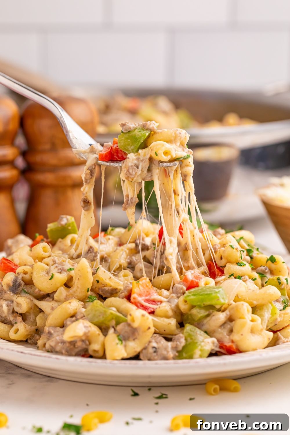 Creamy Philly Cheesesteak Pasta 12 Philly Cheesesteak Pasta on a plate with a fork full pulling up showing the strings of cheese
