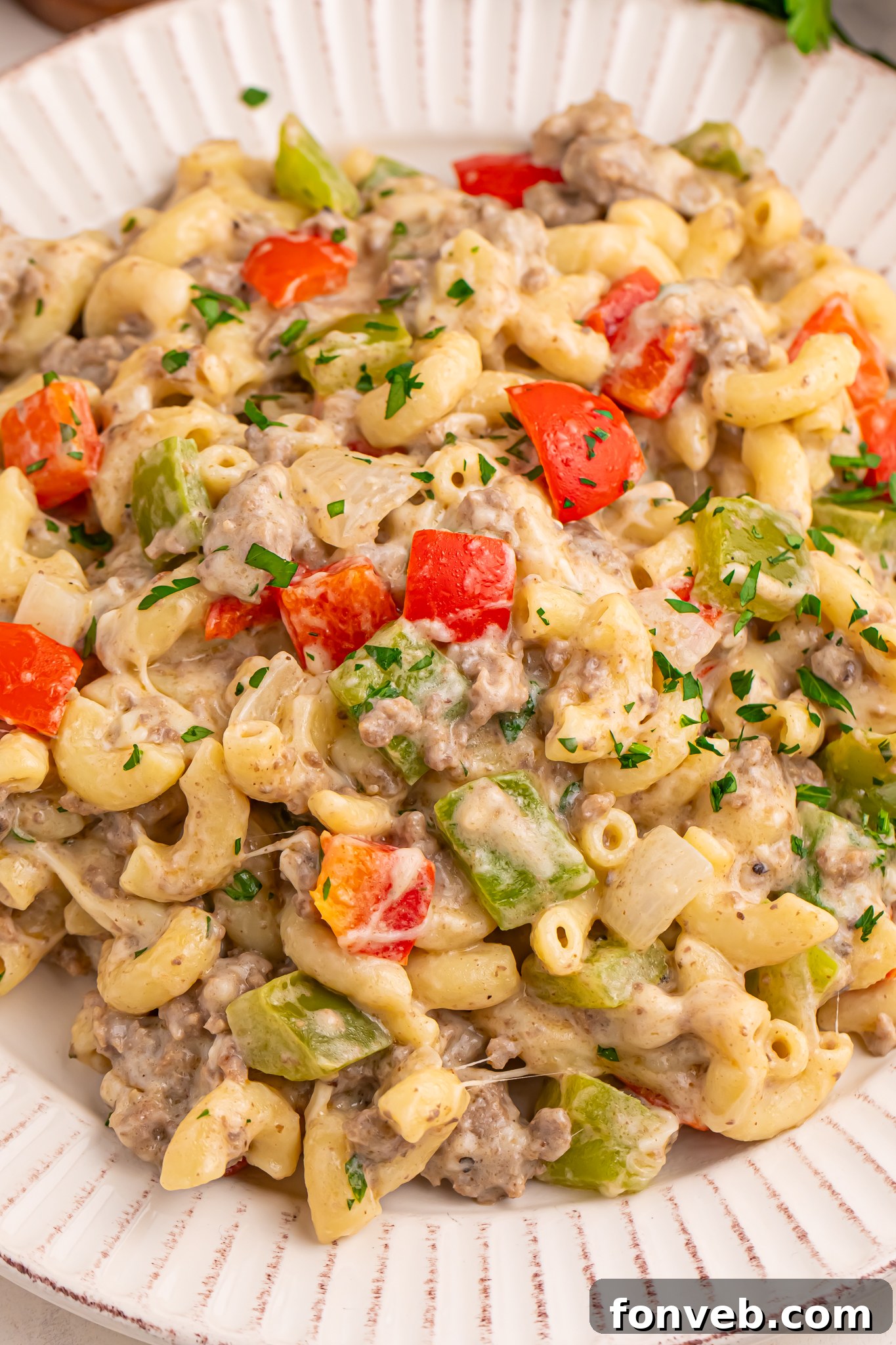 Creamy Philly Cheesesteak Pasta 13 cheese steak pasta on a plate with parsley and cheese around the plate on table
