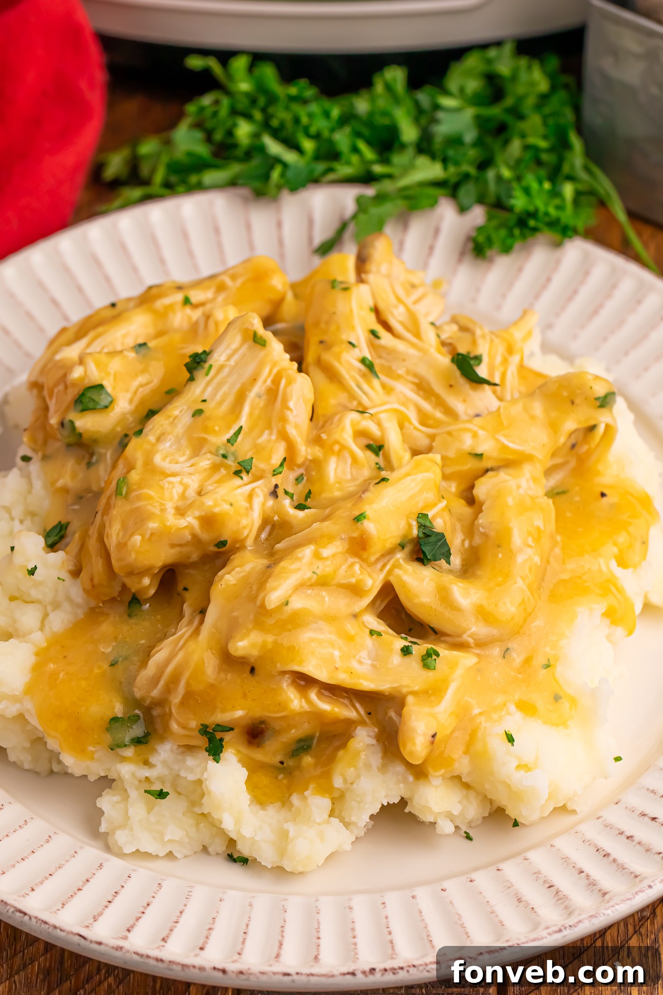 Crock Pot Chicken and Gravy on top of a bed of potatoes on a plate with parsley in the background