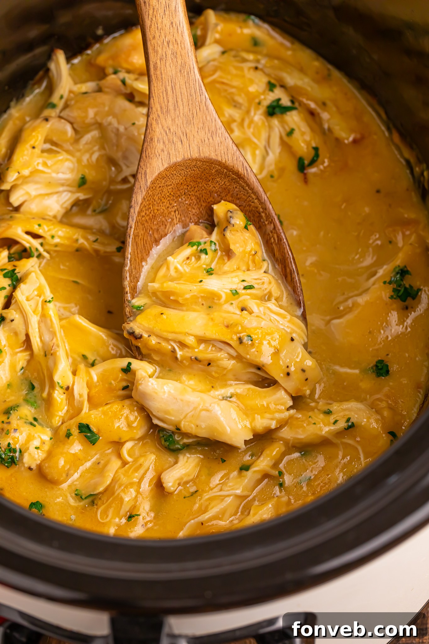 overhead look of crockpot with chicken and gravy in it with a wooden spoon with some meat and gravy on it 