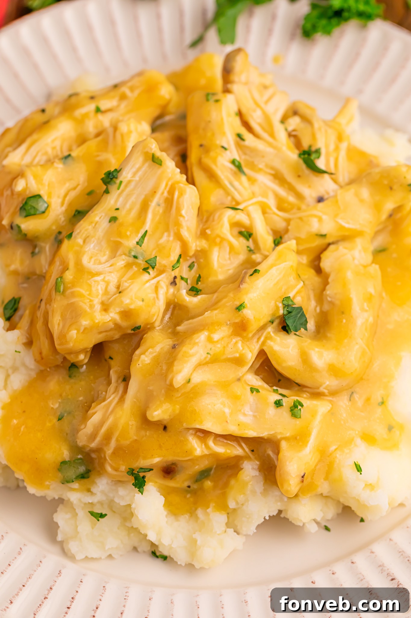 Crock Pot Chicken and Gravy on top of a bed of potatoes on a white plate 