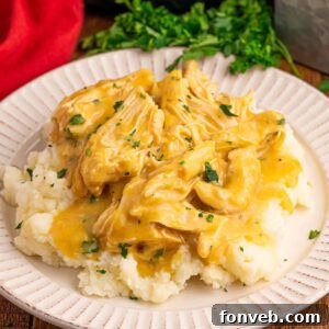 Crock Pot Chicken and Gravy on top of a bed of potatoes on a plate with parsley in the background