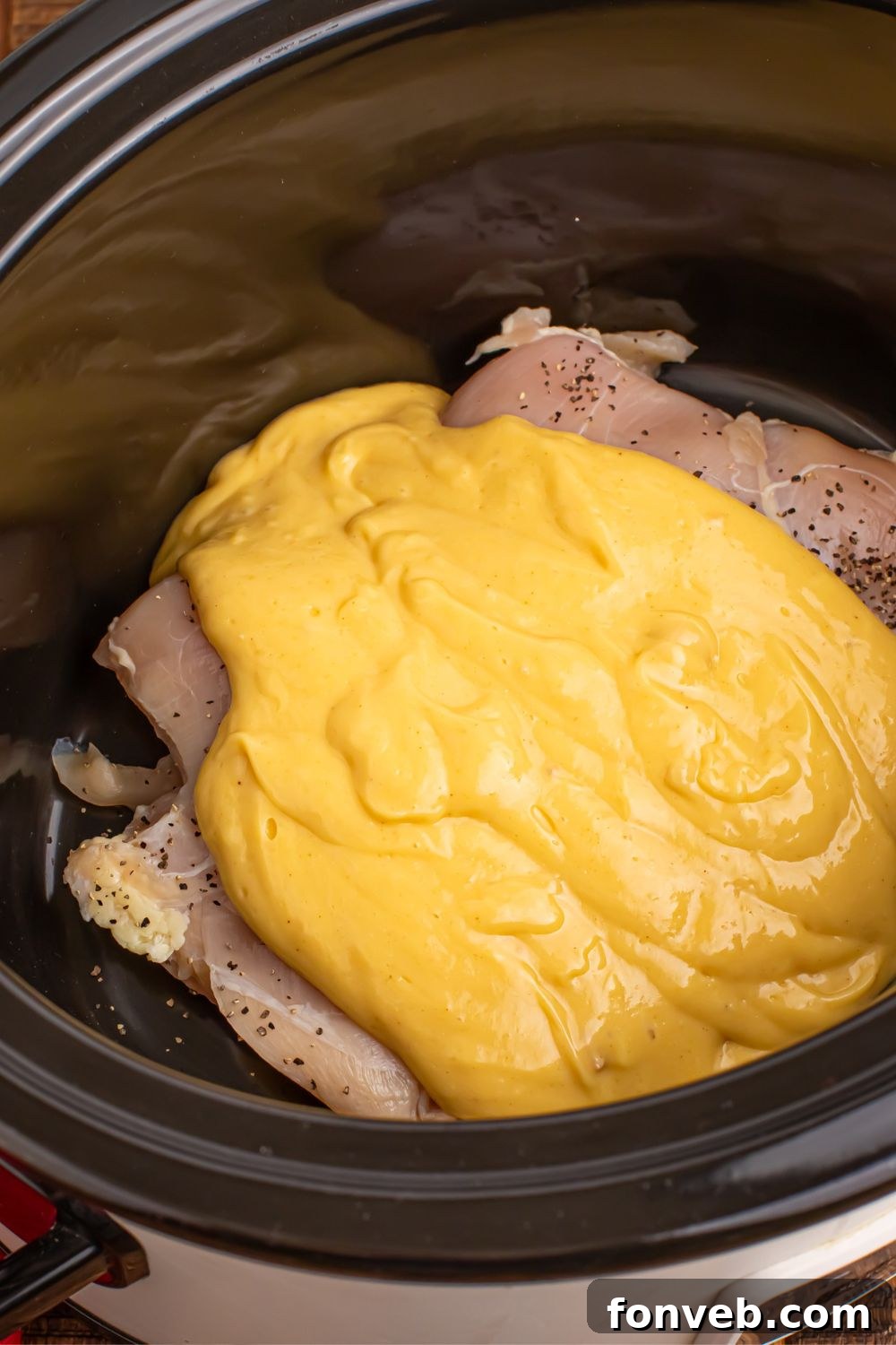 raw chicken in crockpot with a gravy and soup mixture poured over the top of the chicken