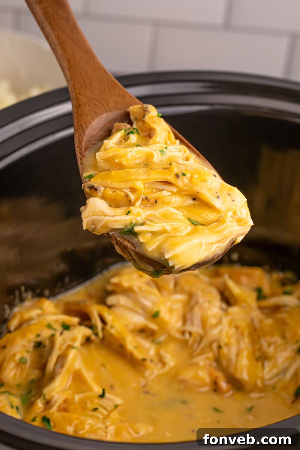 Chicken and Gravy in a crockpot with a wooden spoon full of chicken and gravy 