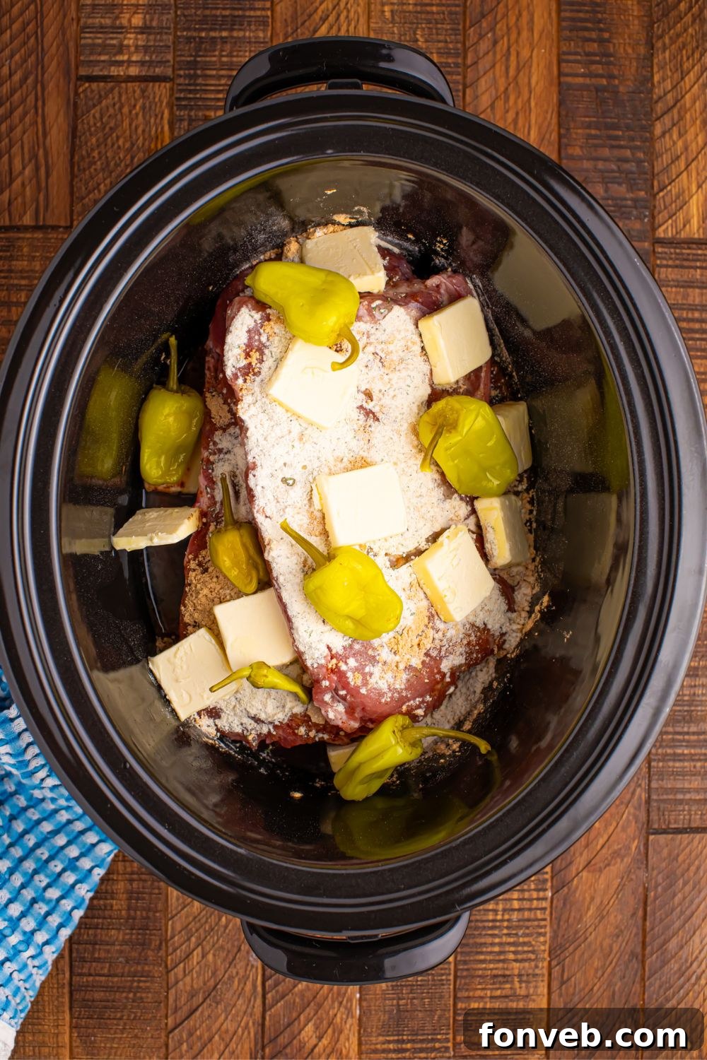 raw ribs in slow cooker topped with seasonings, pepper, and slabs of butter
