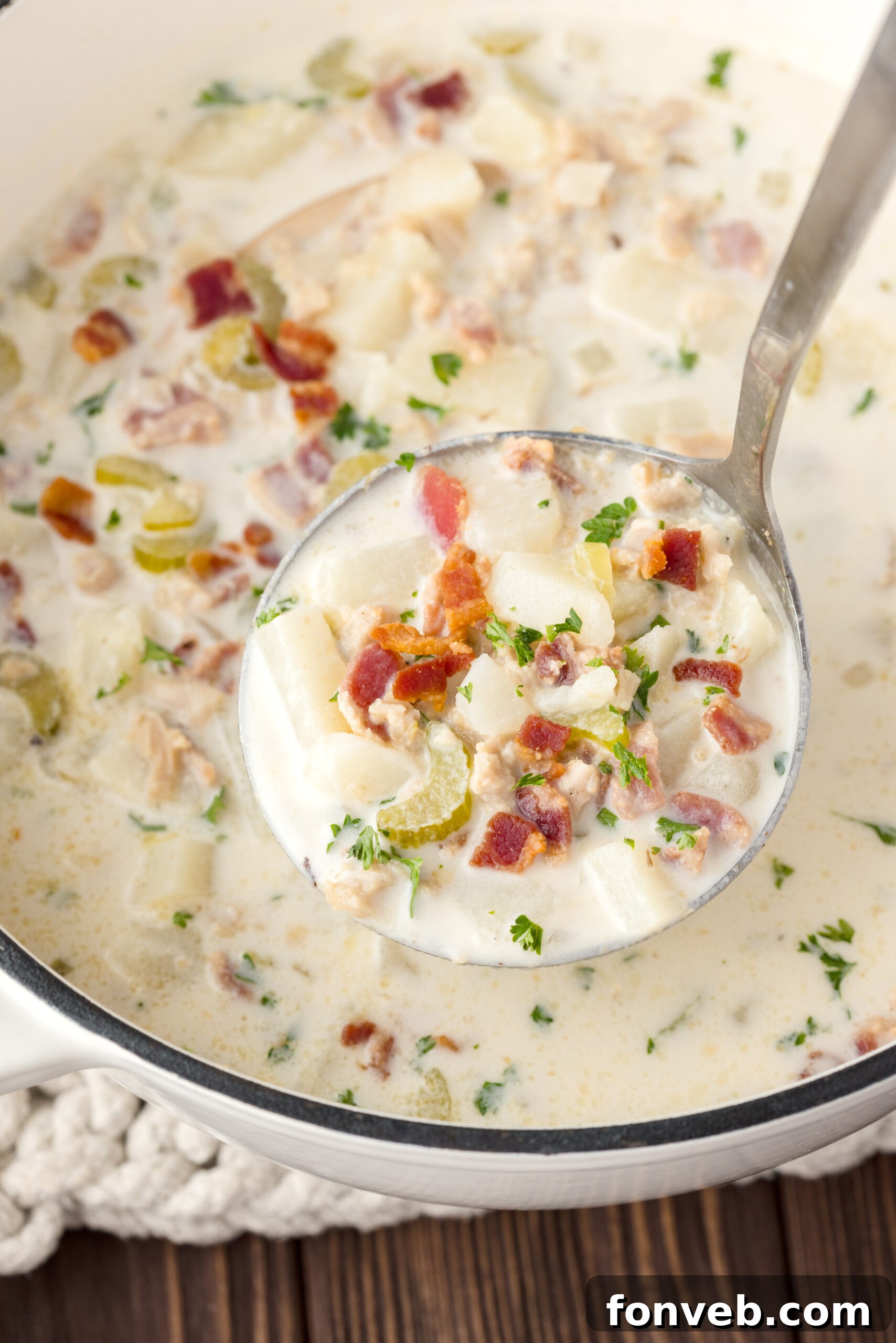 ladle of clam soup above the pot sitting on the table