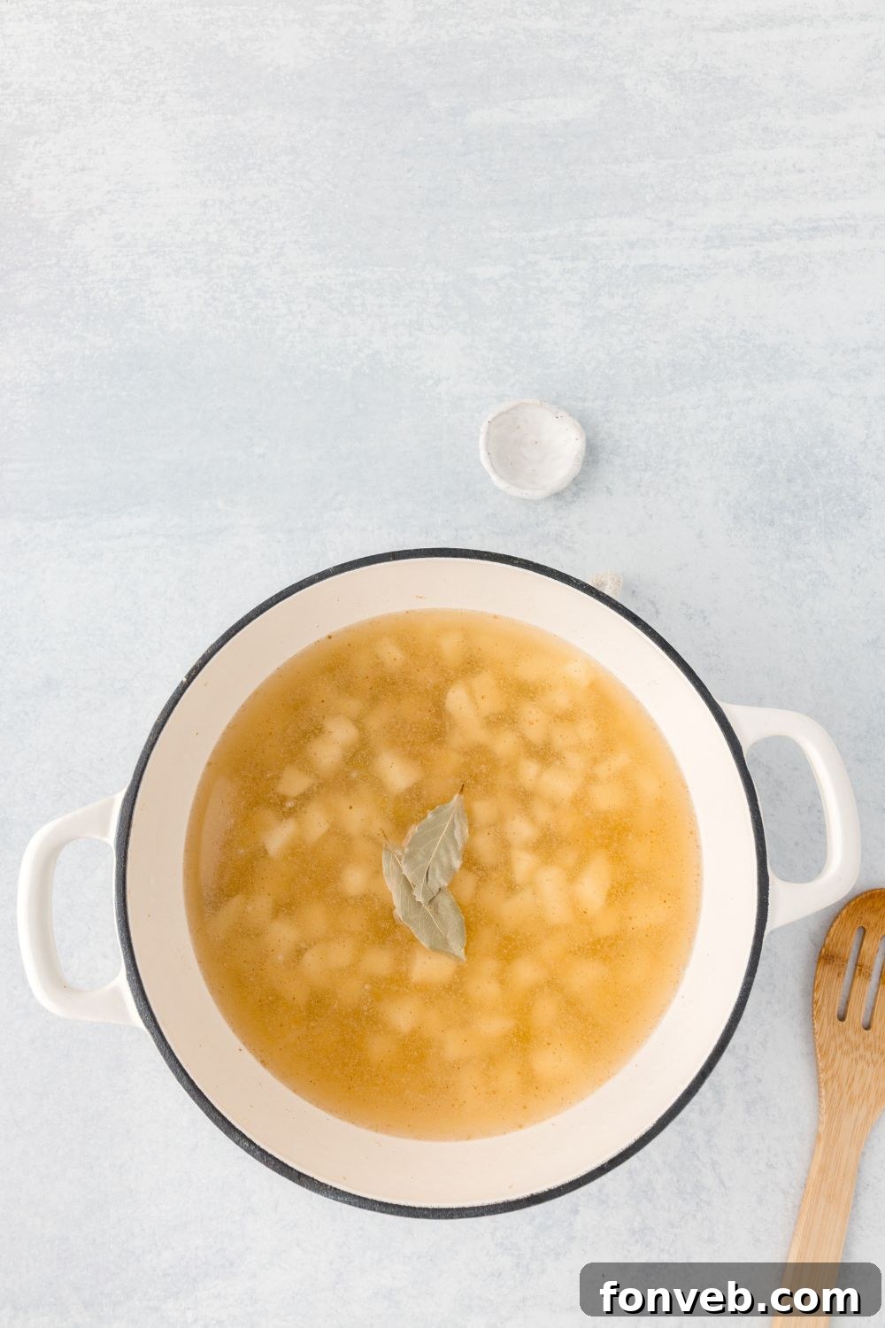 diced potatoes and broth mixture in a dutch oven with two bay leaves sitting on top 