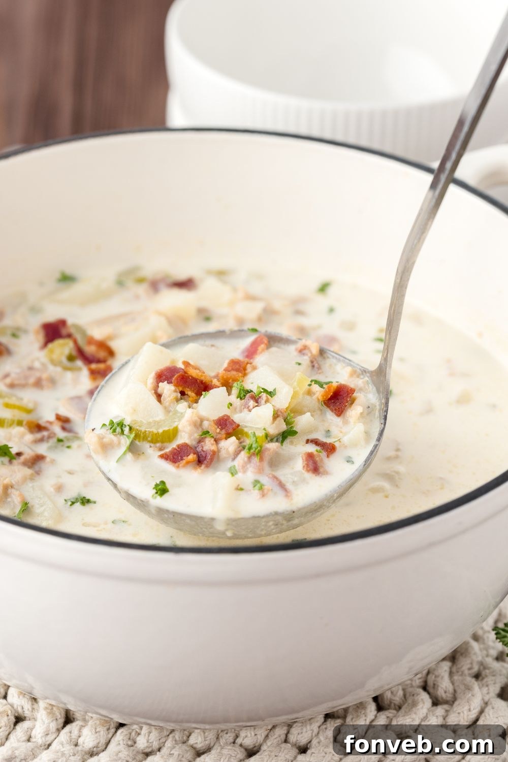 ladle full of clam chowder and a pot under full of chowder as well sitting on table