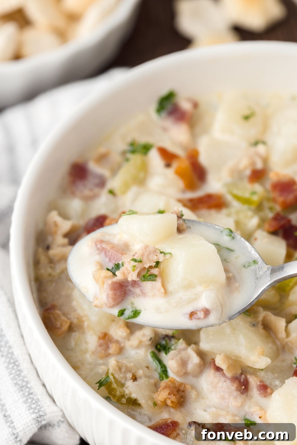 bowl of New England Clam Chowder on table with a spoonful sitting above bowl to show the soup closer 