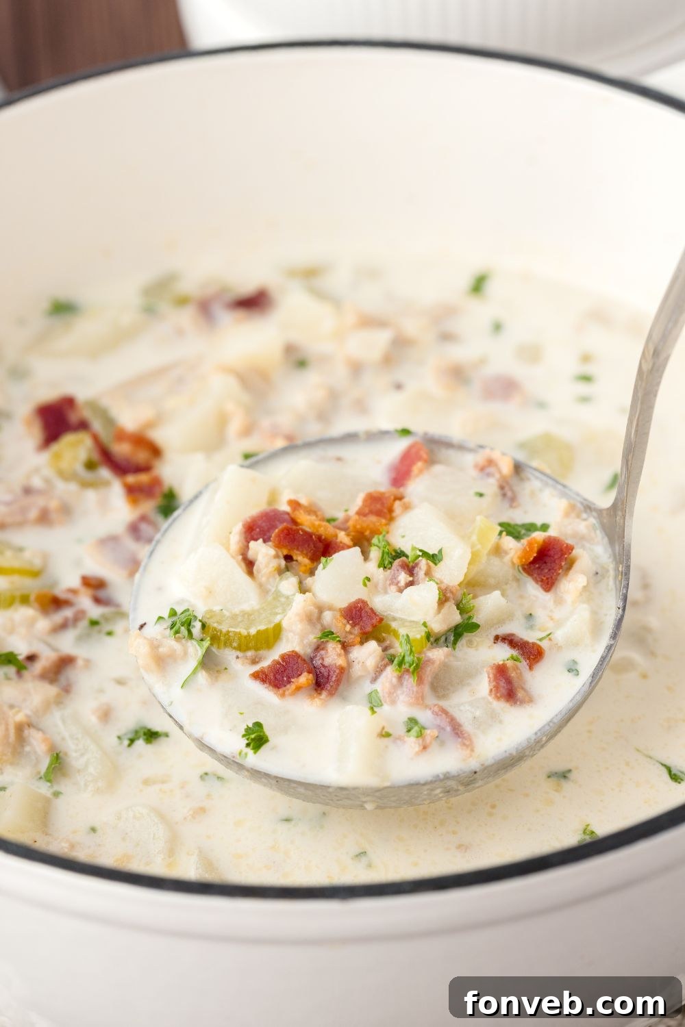 ladle of clam soup above the pot sitting on the table