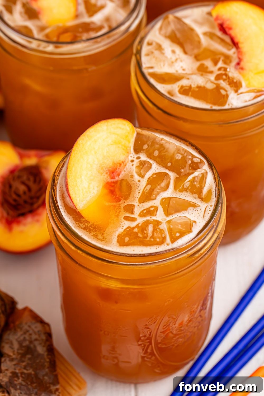 Peach Sweet Tea in mason jars with fresh peach slices in each glass sitting on top of the ice 