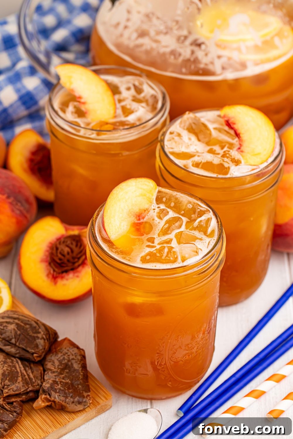 Peach Sweet Tea in a pitcher on table with 3 glasses in front of it, with tea bags, sliced peaches and more around it 