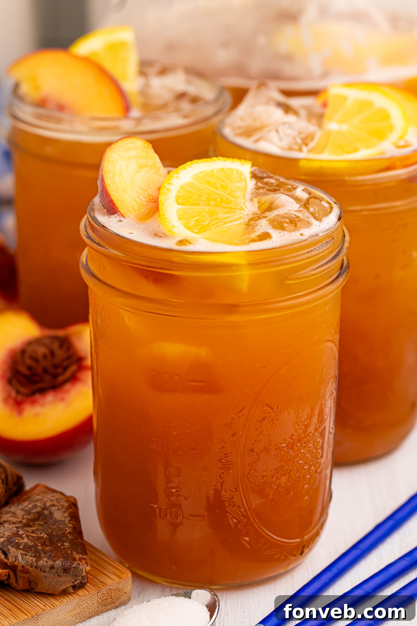 side view of glass full of peach sweet tea with fruit around the glass on table