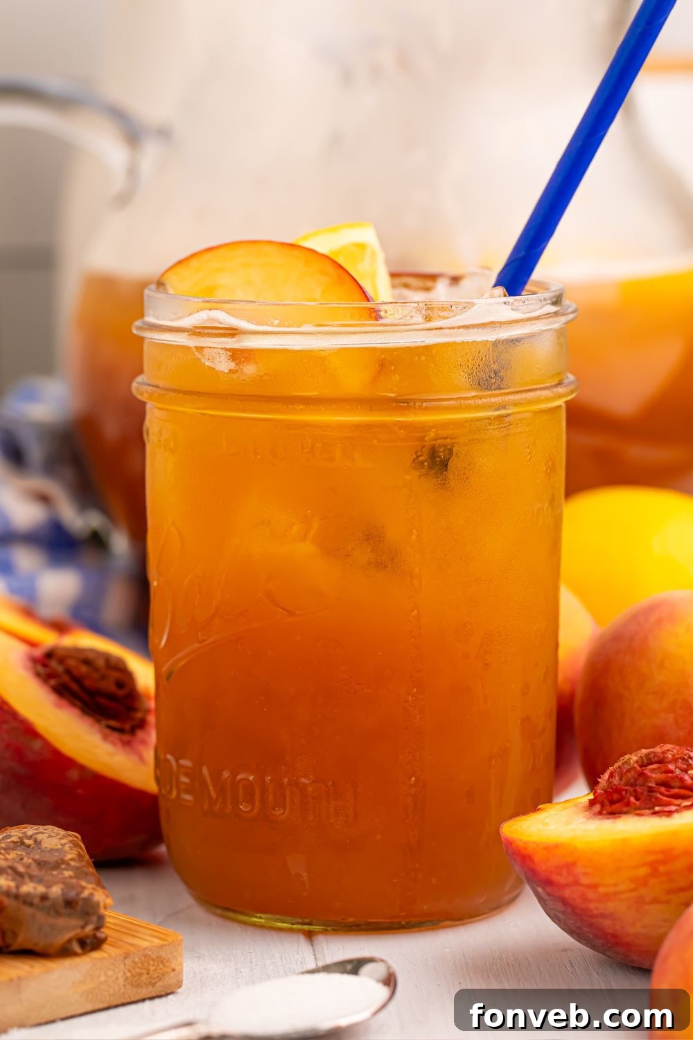side view of glass full of peach sweet tea with fruit around the glass on table