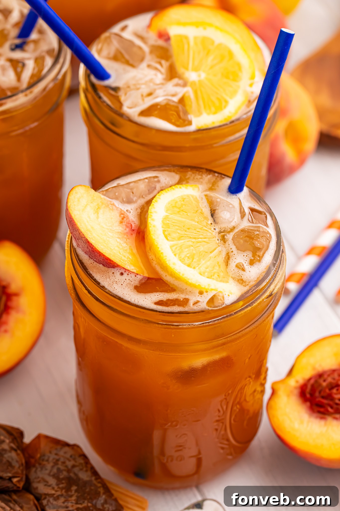 side view of glass full of peach sweet tea with fruit around the glass on table