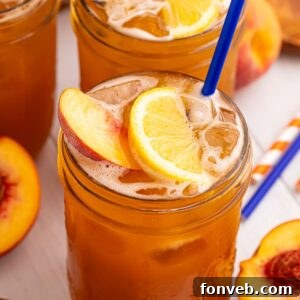 Peach Sweet Tea in mason jars sitting on table and garnished with a lemon wedge, peach slice, and a blue straw