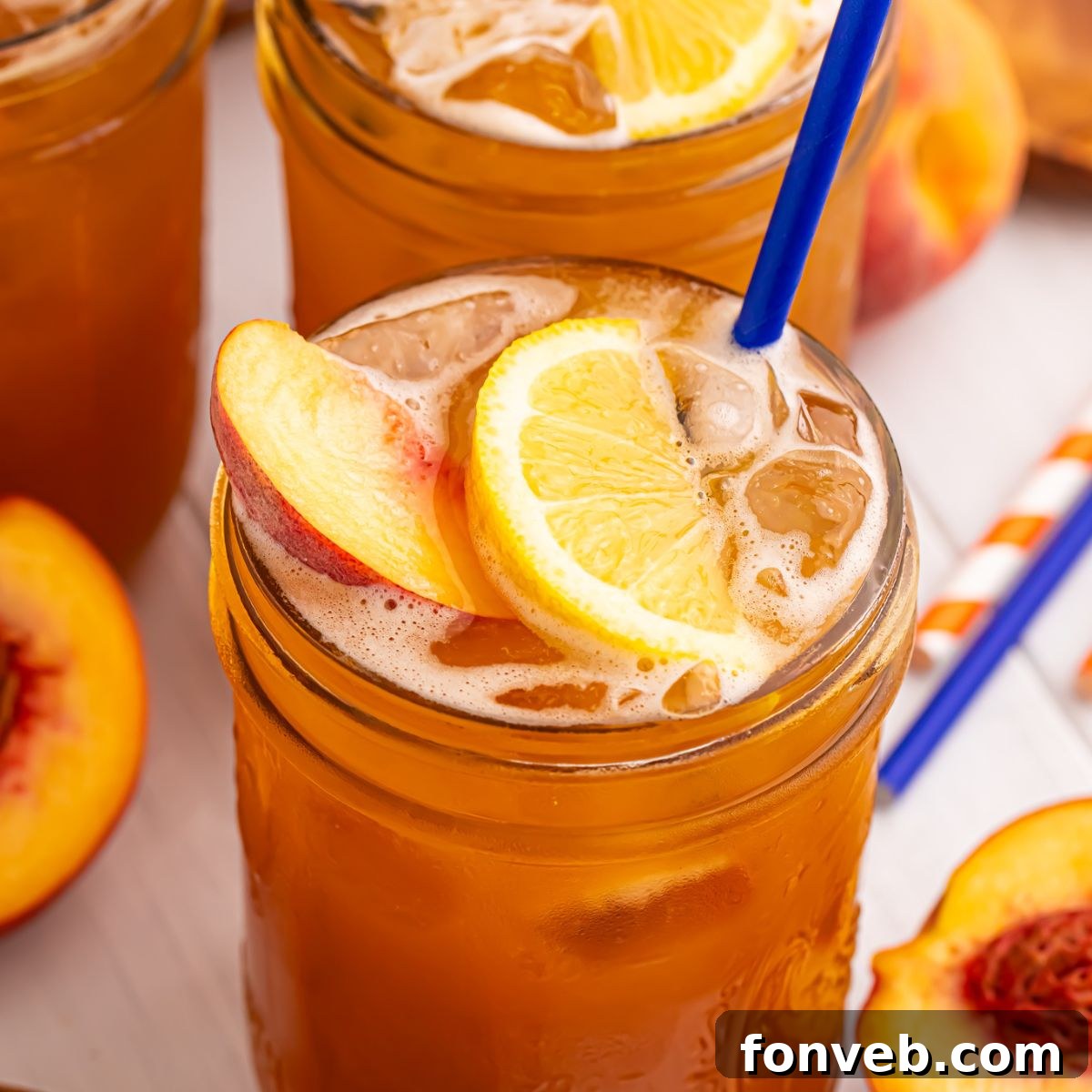 Peach Sweet Tea in mason jars sitting on table and garnished with a lemon wedge, peach slice, and a blue straw 