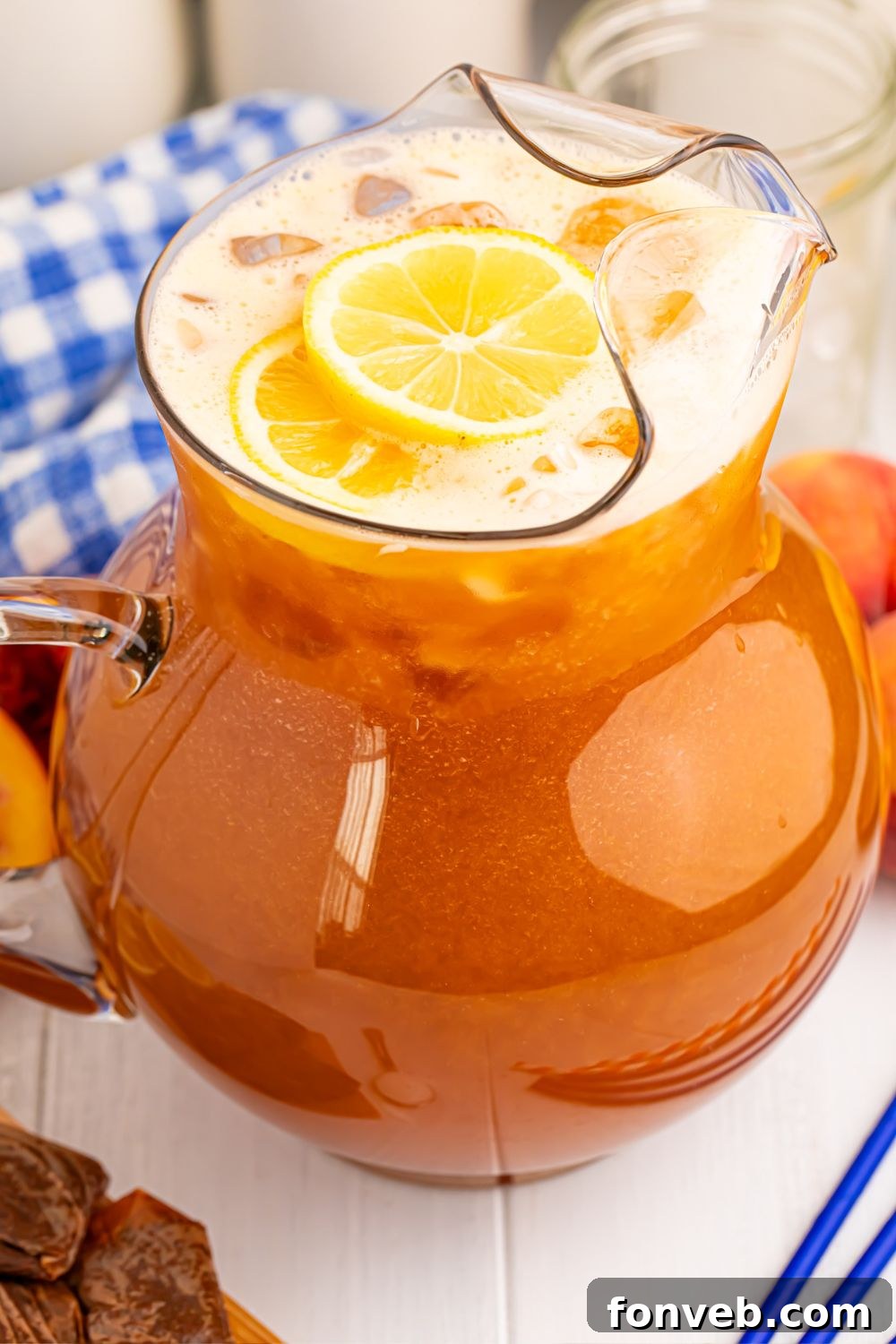 Peach Sweet Tea in a large pitcher on table with a blue napkin and blue straws beside it 